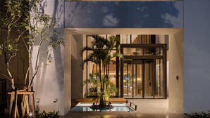 A modern building entrance with a glass door, a small pool, and a palm tree. - Nest Hotel Naha Kumoji (Naha)