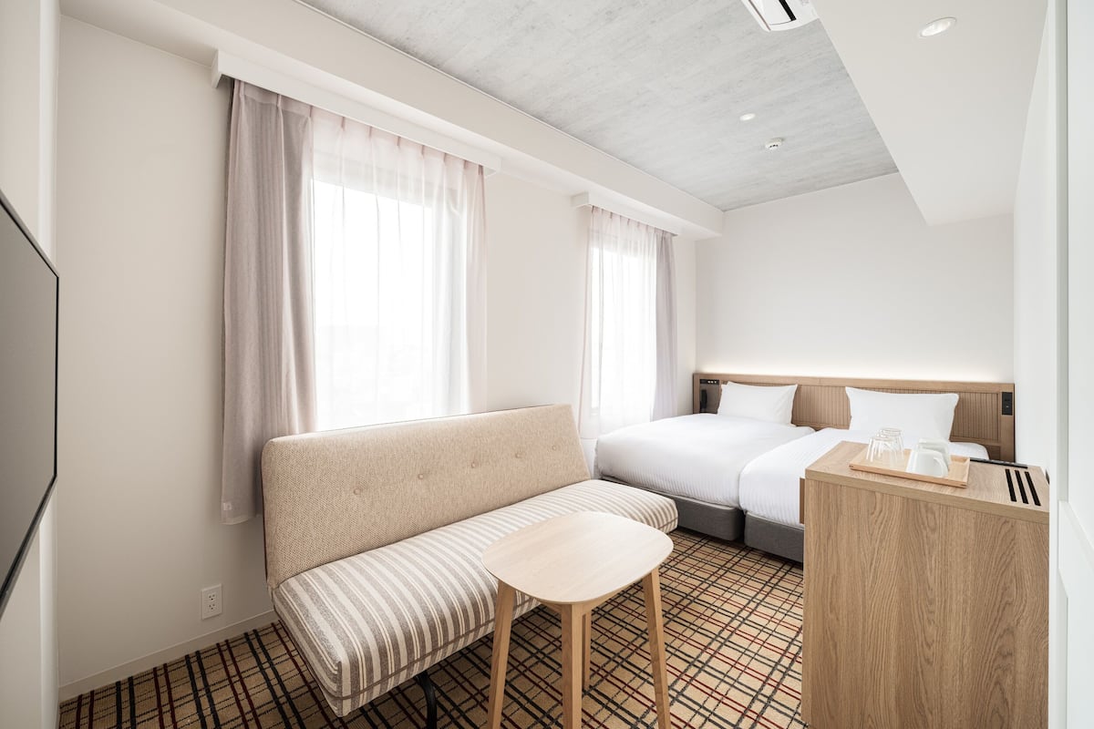 A hotel room with a sofa, a small table, a bed, and a wooden desk with a tray.