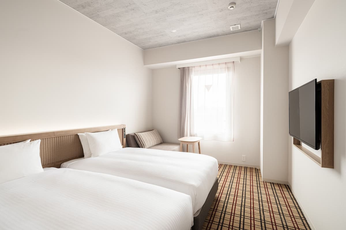 A hotel room with two beds, a television, a small table, and a window with curtains.