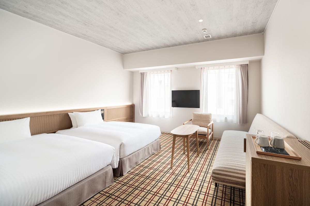 A hotel room with two beds, a TV, a small table with a tray, and a sofa.