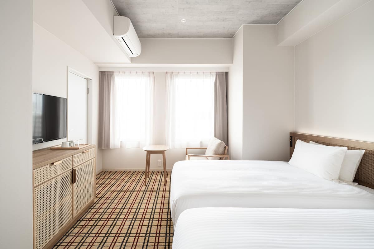 A hotel room with two beds, a TV, a small table, and a window with curtains.