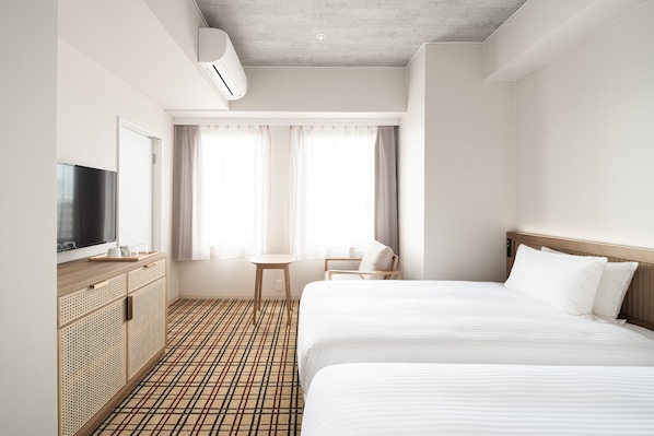 Une chambre d’hôtel avec deux lits, une télévision, une petite table et une fenêtre avec des rideaux.