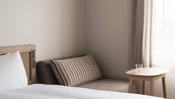 A neatly arranged hotel room with a bed, a bedside table with two glasses, a pillow, and a window with curtains.
