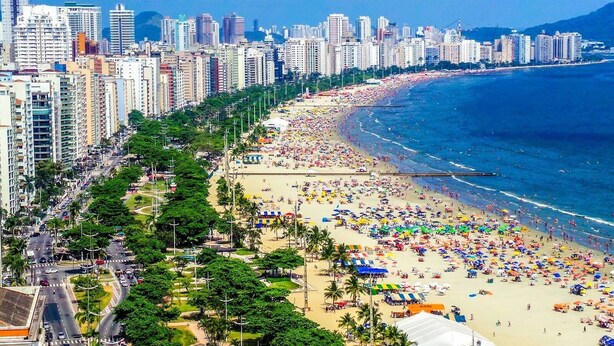 A coastal cityscape with a densely populated beach area, high-rise buildings, and a clear view of the ocean. - Ed. Fte. Gonzaga beach 14and sea view (Santos)