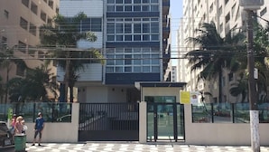 A modern building with a glass facade, a gated entrance, and palm trees in the foreground. - Ed. Fte. Gonzaga beach 14and sea view (Santos)
