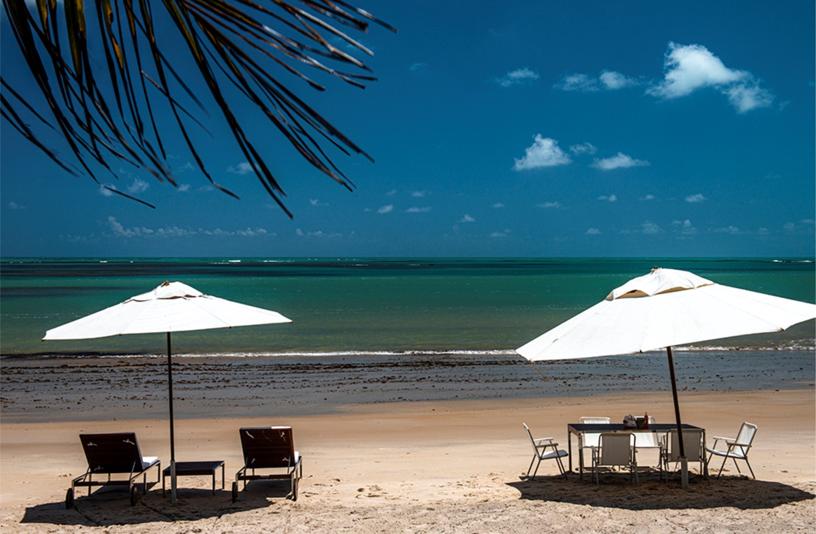 A beach with two white umbrellas, a table, and chairs.