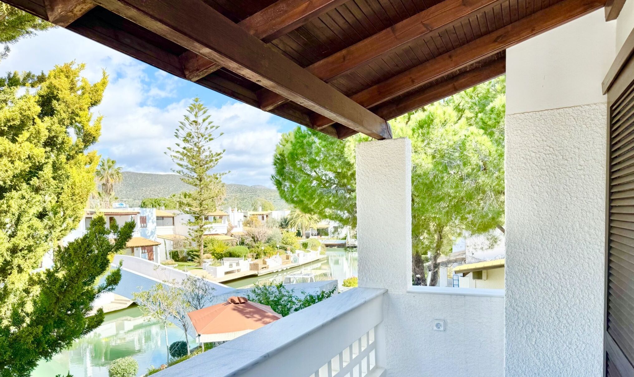 A balcony with a view of a swimming pool, a mountain in the background, and a white building with a textured wall.