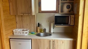 A compact kitchen with wooden cabinets, a built-in microwave, a small refrigerator, and a window above the sink.