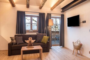 Un salon avec un canapé, une table, une lampe, un téléviseur et une fenêtre avec des rideaux.