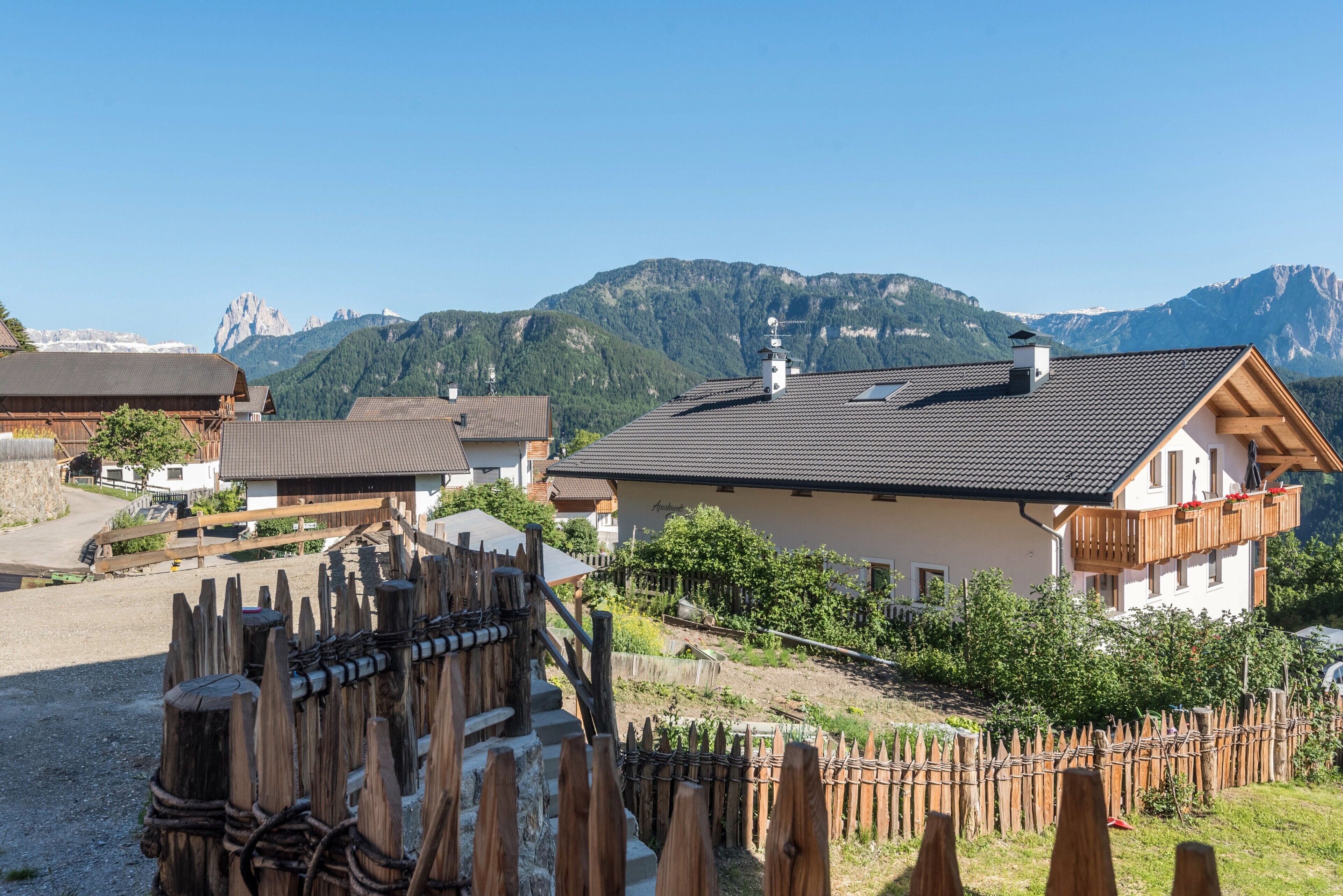 Ein Bergdorf mit traditionellen Holzhäusern, einem Holzzaun und freiem Blick auf die umliegenden Berge.
