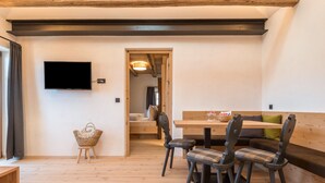 Un plancher en bois, un téléviseur fixé au mur, une table à manger avec des chaises et un canapé.