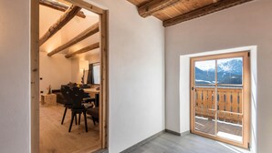 Una stanza con soffitto in legno, un balcone con vista sulle montagne e una porta che dà su un'altra stanza.