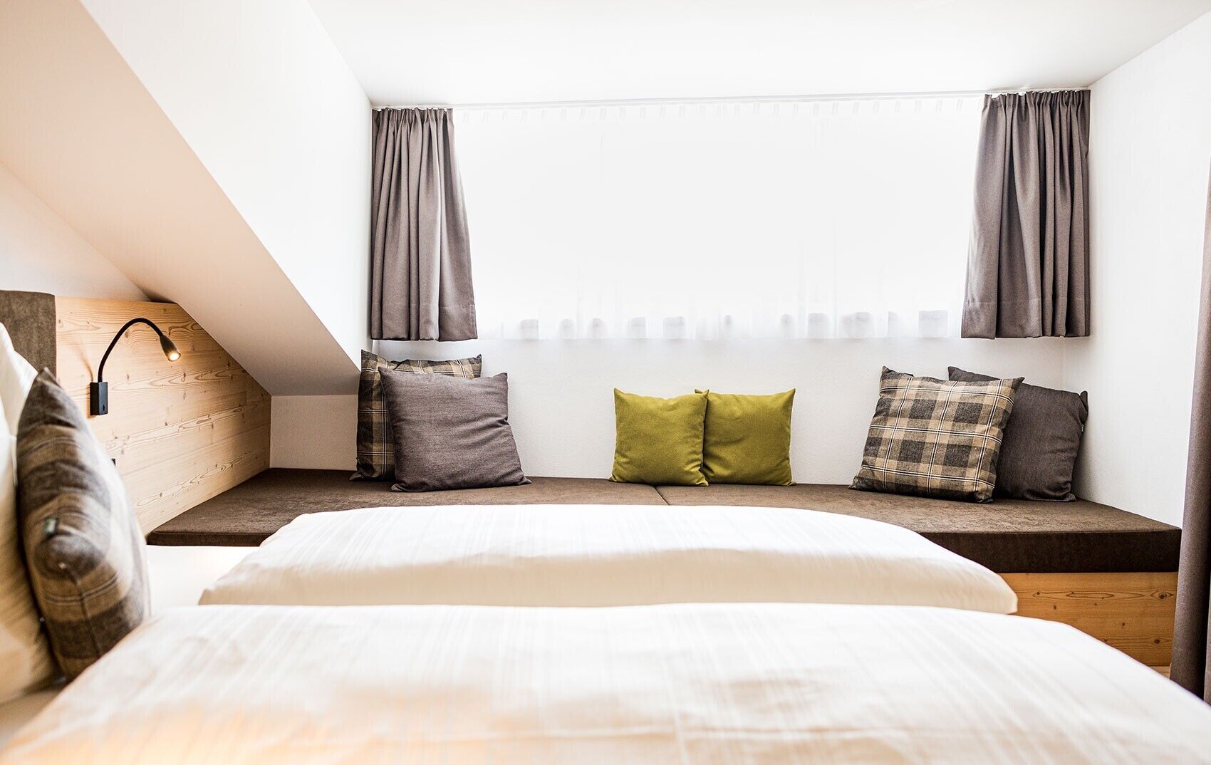 A bedroom with a sloped ceiling, a bed, a bench with pillows, and a wall-mounted lamp.