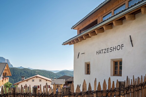 A traditional building labeled 'HATZESHOF' with a wooden fence in front, set against a mountainous backdrop.