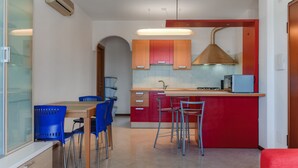 A modern kitchen with a central island, red and orange cabinets, a built-in stove, and blue chairs.
