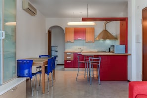 Una cocina moderna con una isla central, armarios rojos y naranjas, una estufa empotrada y sillas azules.