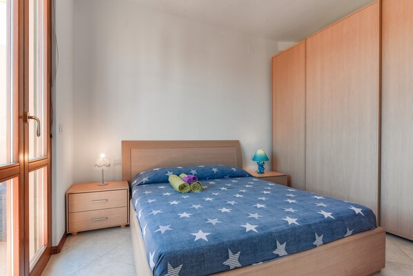 A bedroom with a bed, a nightstand, a lamp, and a wardrobe.