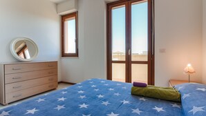 A bedroom with a bed, dresser, mirror, and a window with a view.