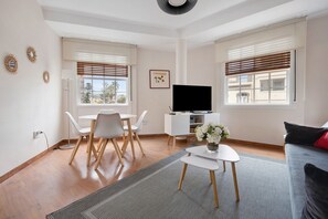 En moderne stue med spiseplads, et fladskærms-tv og en sofa med en rød pude.
