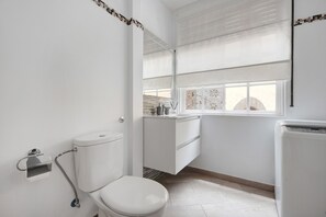 A bathroom with a toilet, a sink, and a window with blinds.