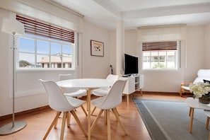 A modern living room with a round dining table, white chairs, a TV, and a sofa.