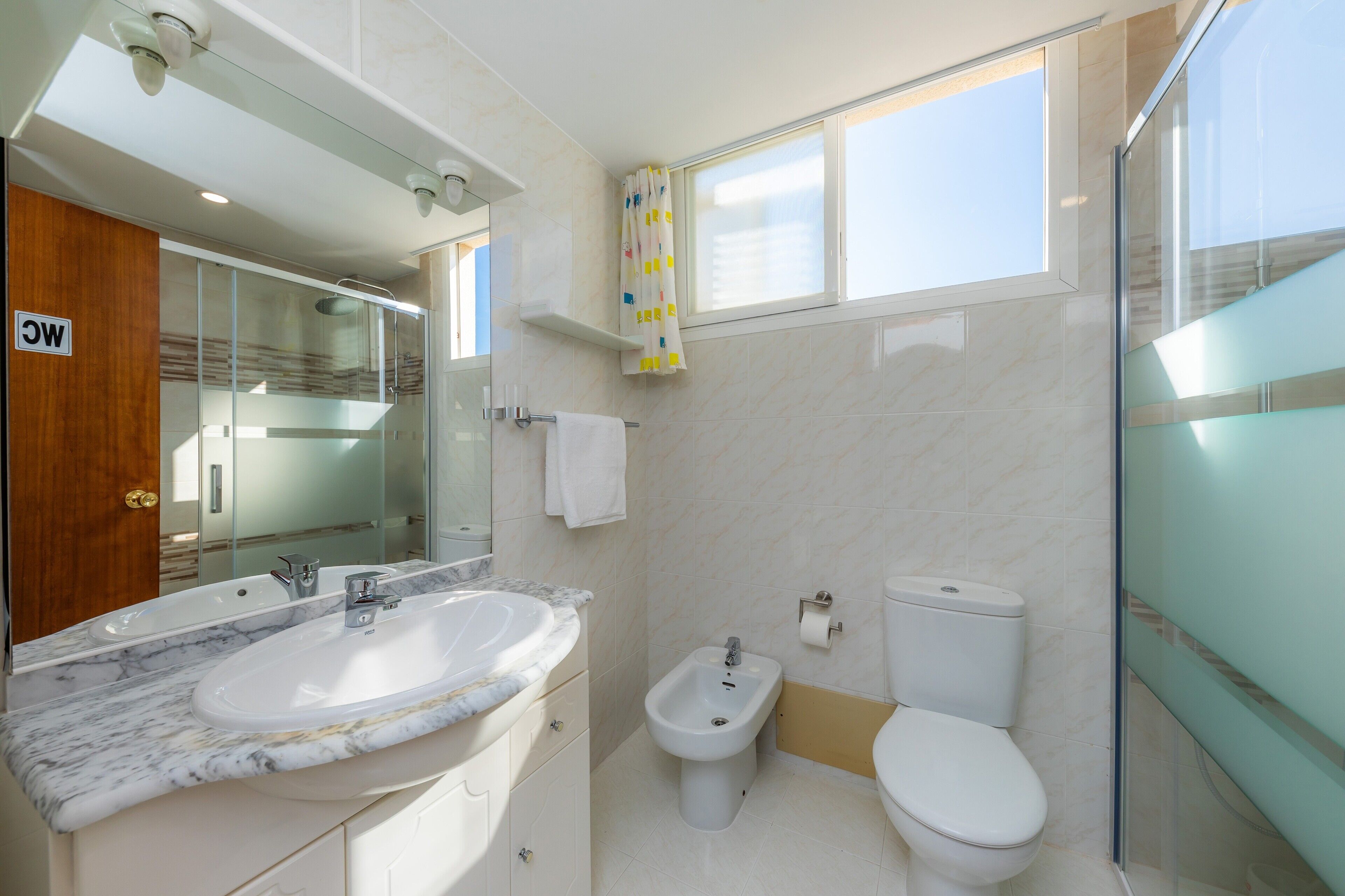 Une salle de bain moderne avec un lavabo en marbre, un bidet, des toilettes et une douche à parois de verre.
