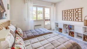 Een slaapkamer met twee bedden, een raam met gordijnen, een boekenkast en een decoratief paneel aan de muur.