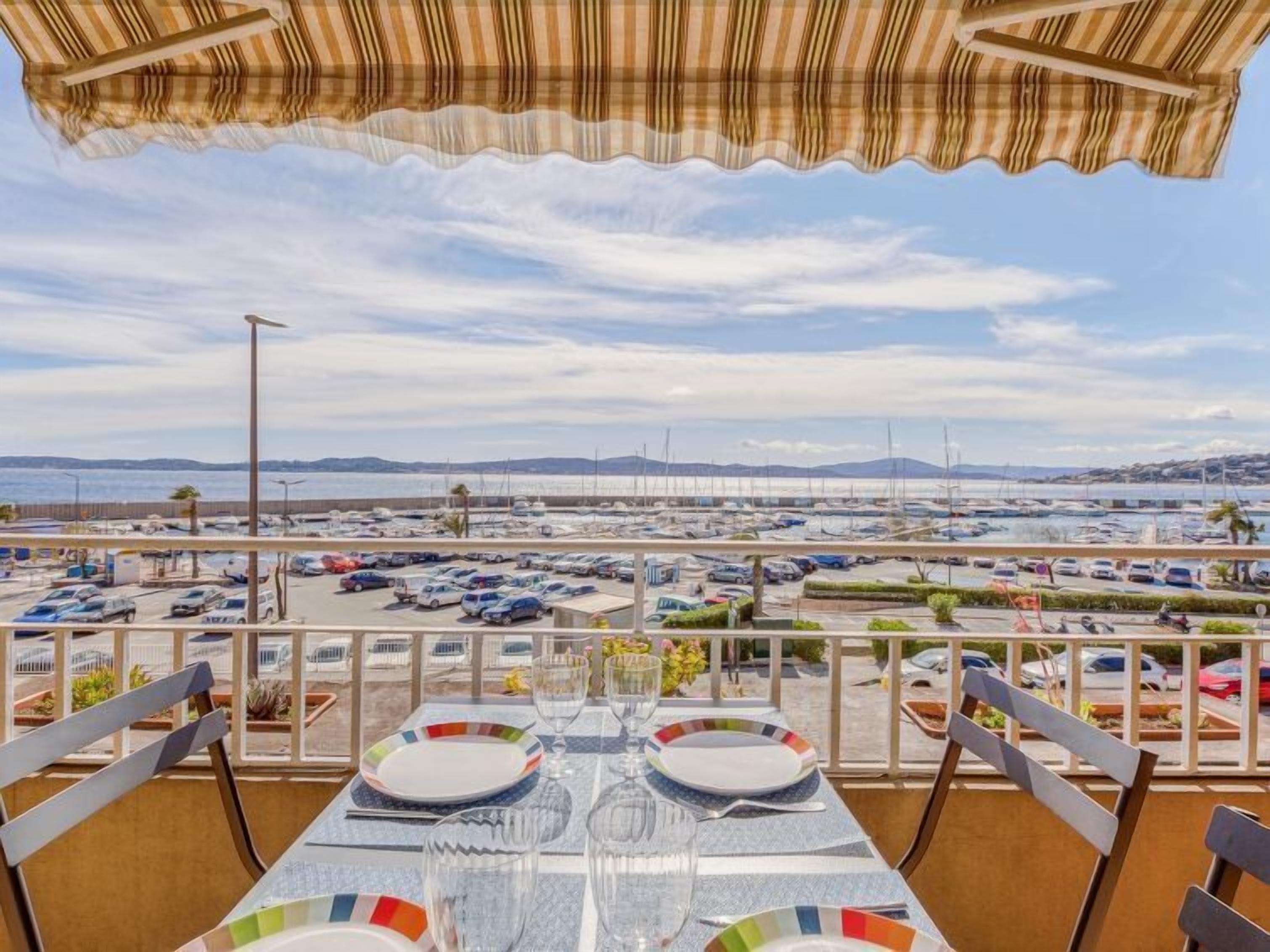 A dining area with a table set for two, overlooking a marina with boats and a parking lot.