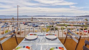 Een eethoek met een tafel gedekt voor twee personen, met uitzicht op een jachthaven met boten en een parkeerplaats.