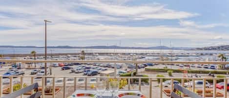 A dining area with a table set for two, overlooking a marina with boats and a parking lot.