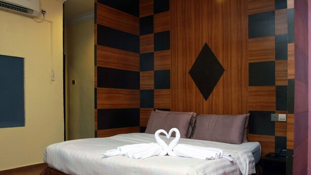 A hotel room with a bed, a wall with a geometric pattern, and a heart-shaped towel arrangement. - GD Hotel - Permas Jaya (Masai)