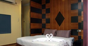 Une chambre d’hôtel avec un lit, un mur orné d’un motif géométrique et une serviette pliée en forme de cœur.