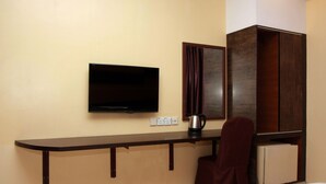 A hotel room with a flat-screen TV mounted on the wall, a wooden cabinet, a desk with a chair, and a coffee maker. - GD Hotel - Permas Jaya (Masai)