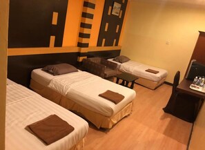 A hotel room with three single beds, a small sofa, a desk with a chair, and a wall with a geometric pattern. - GD Hotel - Permas Jaya (Masai)