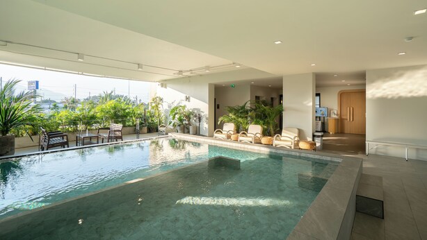 An indoor swimming pool with clear water, surrounded by lounge chairs and potted plants. - The Rise Suites Hotel Chiang Mai  (Chiang Mai)