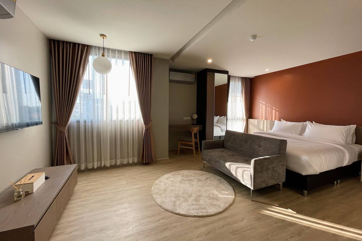 Une chambre d’hôtel moderne avec un lit, un canapé, un tapis rond et un bureau avec une lampe.