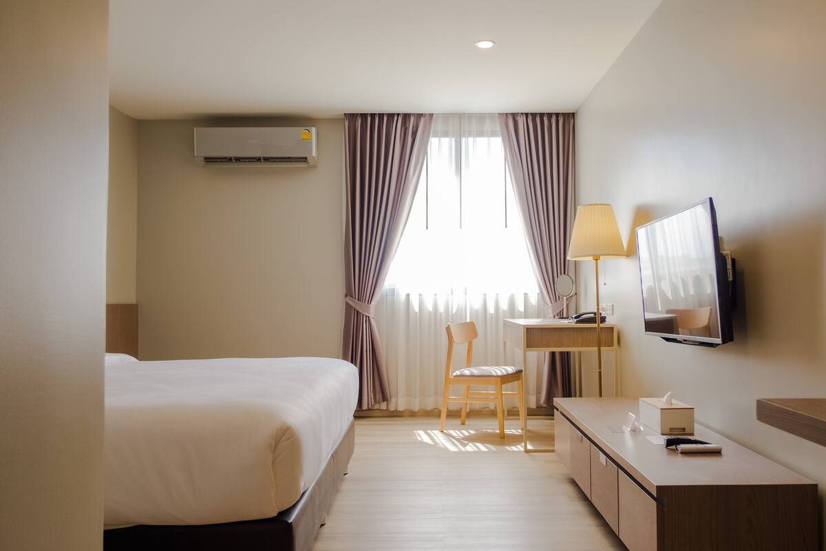 Une chambre d’hôtel comprenant un lit, un bureau avec une lampe, une chaise, un téléviseur et un appareil de climatisation.