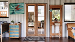 Une pièce avec une porte en bois, une commode bleue à tiroirs, un canapé en osier et un tableau représentant une libellule.