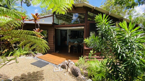 A modern house with a wooden deck, surrounded by lush greenery and tropical plants.