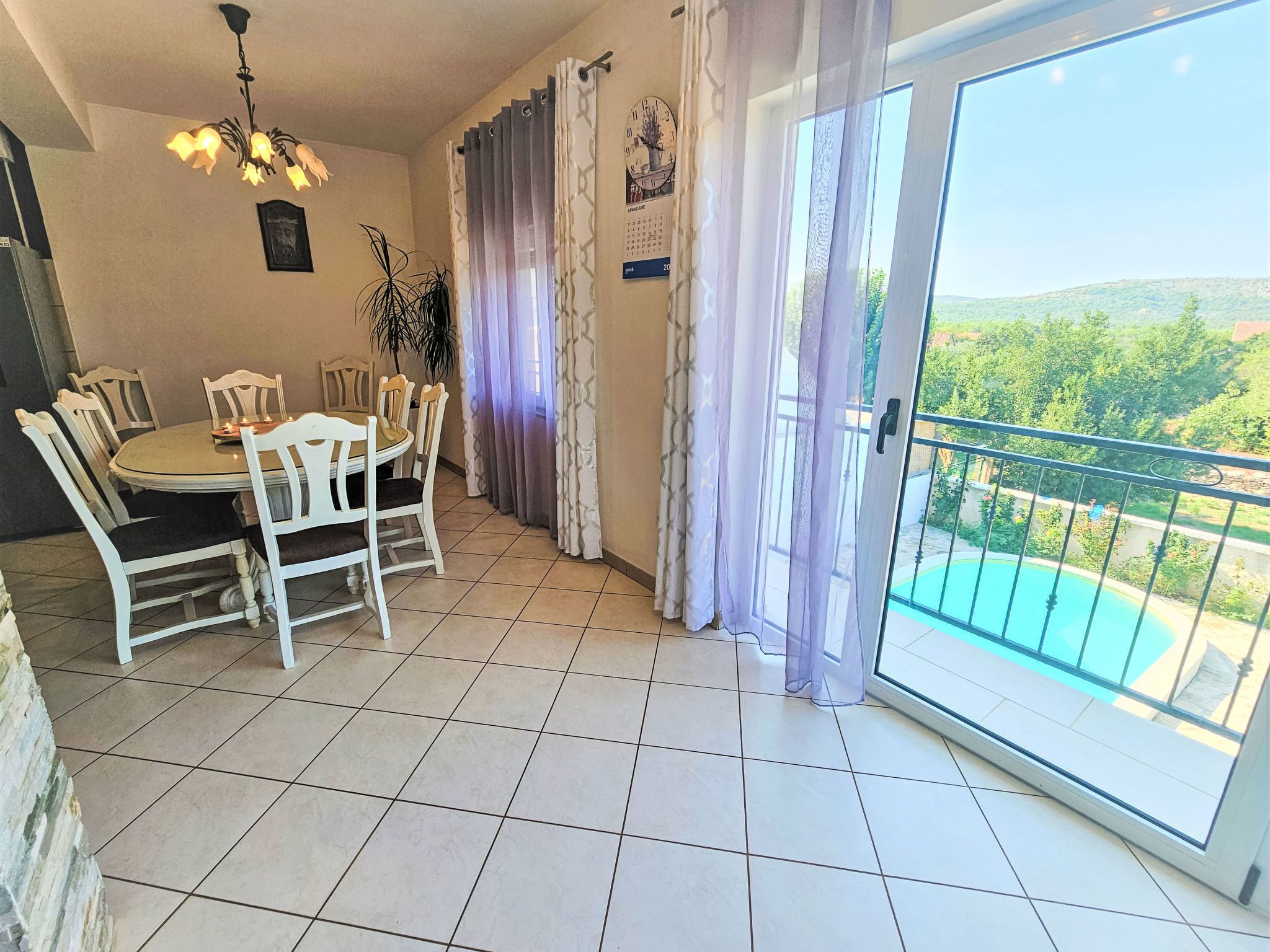 Un comedor con una mesa redonda y sillas, una araña y vistas a una piscina a través de una puerta de cristal.