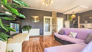 A modern living room with a purple sofa, a wooden floor, a large window, and a kitchen area. - Joy on Countryside by Interhome (Šibenik/Dubrava)
