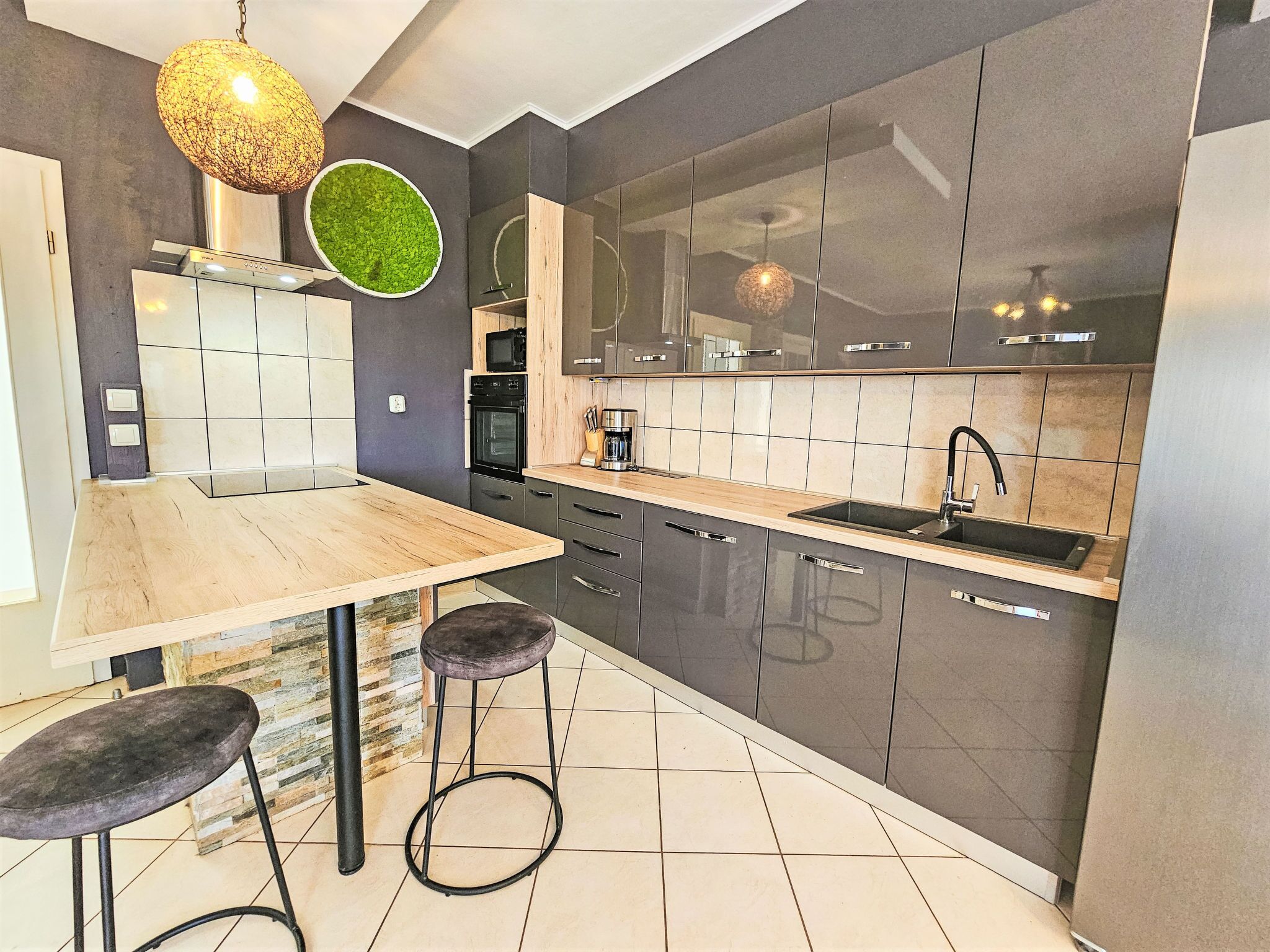 Eine moderne Küche mit einem Holztisch, zwei Barhocker, einem Backofen und einem großen Fenster.