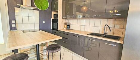 Eine moderne Küche mit einem Holztisch, zwei Barhocker, einem Backofen und einem großen Fenster.