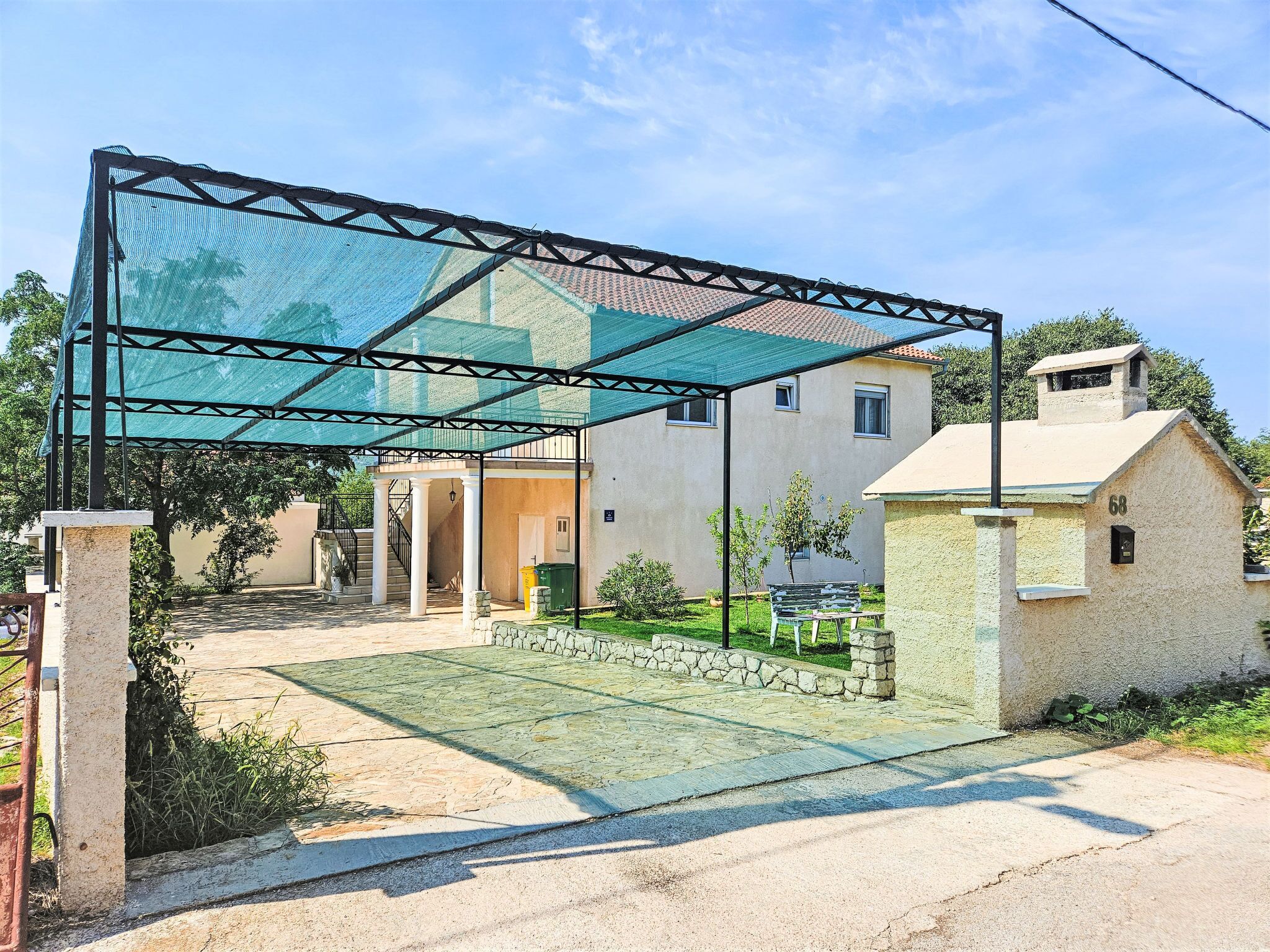 Un espace extérieur abrité, doté d’une pergola, d’un chemin en pierre et d’un petit bâtiment portant le numéro 68.
