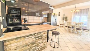 A modern kitchen with a central island, built-in appliances, and a dining area with a chandelier. - Joy on Countryside by Interhome (Šibenik/Dubrava)