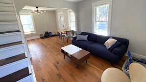 Un salón espacioso con pisos de madera, un sofá azul oscuro, una mesa de centro de madera y un comedor con una mesa y sillas.