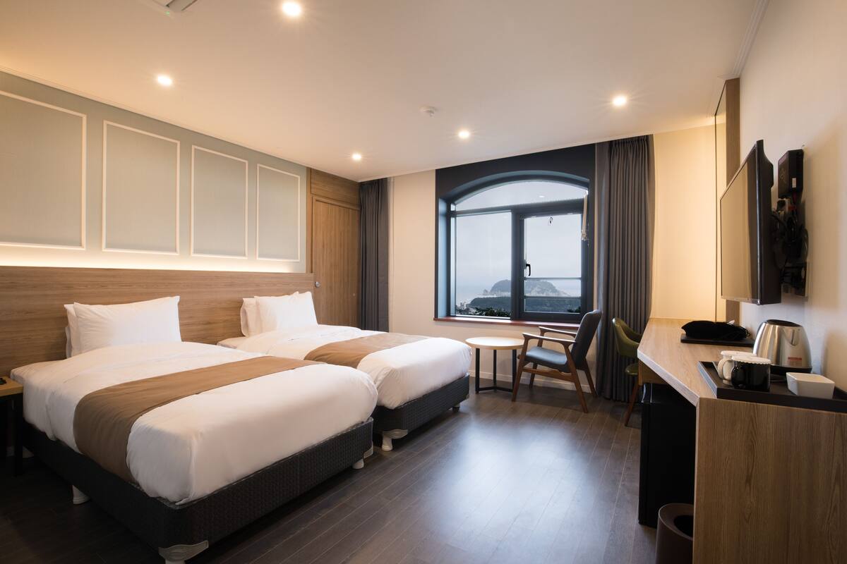 A hotel room with two beds, a desk, a chair, a window with a view, and a TV.