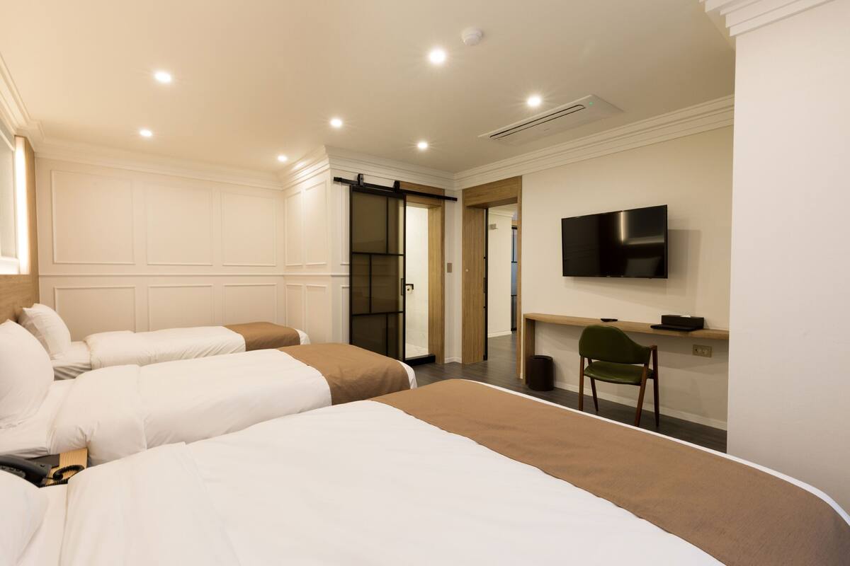 A hotel room with two beds, a desk, a chair, a television, and a sliding door leading to a bathroom.