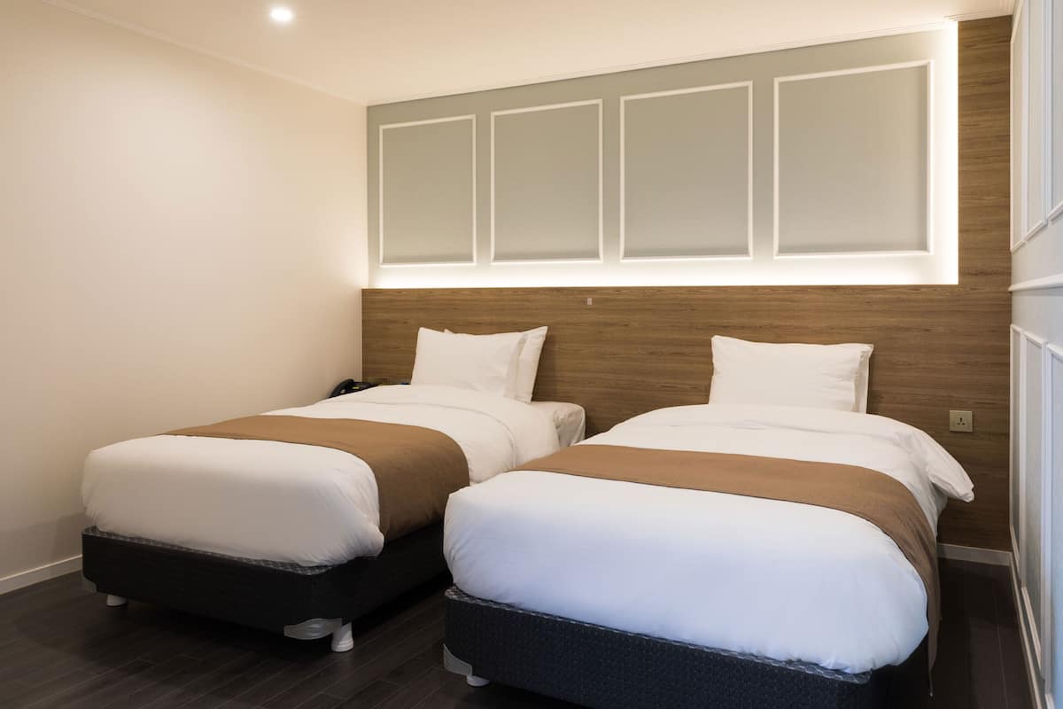A hotel room with two beds, a wooden headboard, and a window with a view.