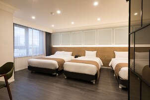 Habitación de hotel con tres camas, un ventanal grande con cortinas y un diseño moderno.